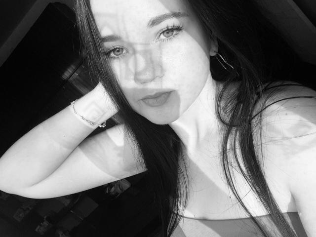 RoxyVesper has long dark hair, light skin, and wears a strapless top. Her shadowed face, hoop earrings, and bracelet are visible. She's looking at the camera with a serious expression.
