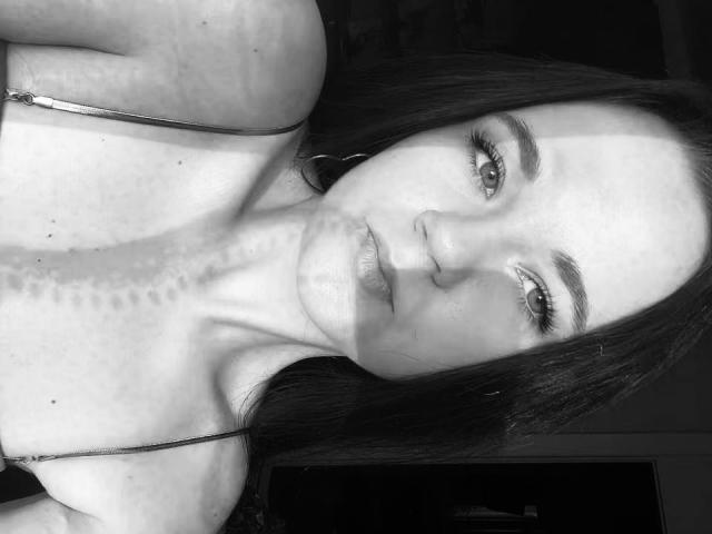 black and white selfie of RoxyVesper with dark hair, wearing a spaghetti strap top, showing a tattoo on her neck, with her lips slightly parted and looking at camera.
