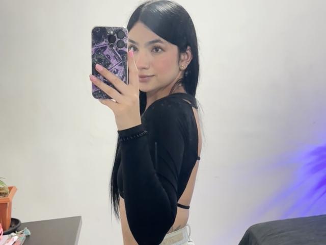 EvaaFarix with long black hair, wearing a black long-sleeve top, showing her back and a hint of her tits, taking a mirror selfie with a purple phone case.
