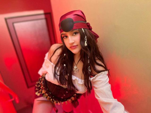 IrisBlair with long dark hair, wearing a red headband with an eye patch, white off-shoulder top, and brown corset, kneeling with a chain necklace, red and yellow background.