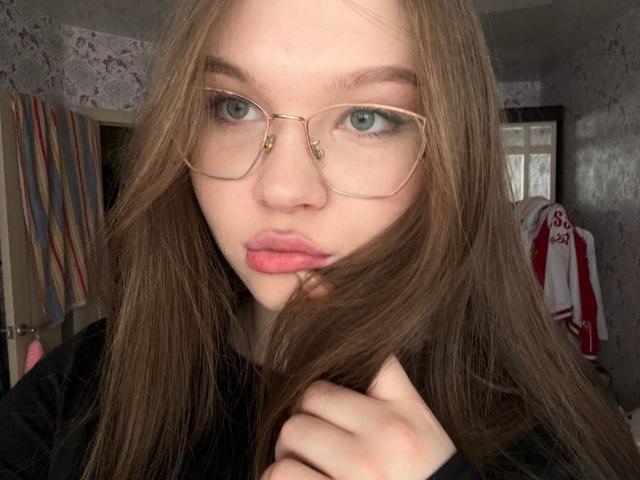 Yolando Waldren, con lunghi capelli castani, labbra rosate e occhi azzurri, indossa occhiali con montatura dorata, una camicia nera e si tiene i capelli, guardando nella fotocamera. Le sue natiche non sono visibili..