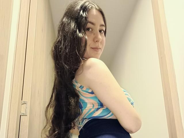 MabyLegrand with long wavy brown hair, wearing a blue and white striped top, looking over her shoulder, showing her small ass in tight blue pants.