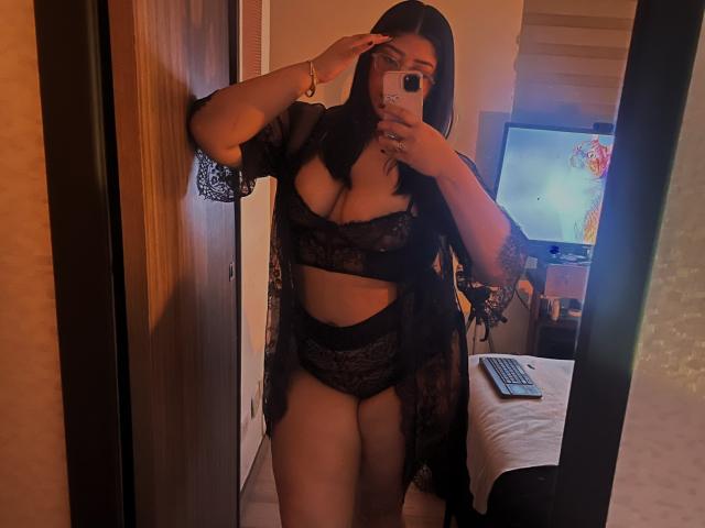 AlexaKiim with dark hair, wearing black lace lingerie and sheer robe, holding phone, covering eye, mirror selfie, showing her tits and ass, in dimly lit room.