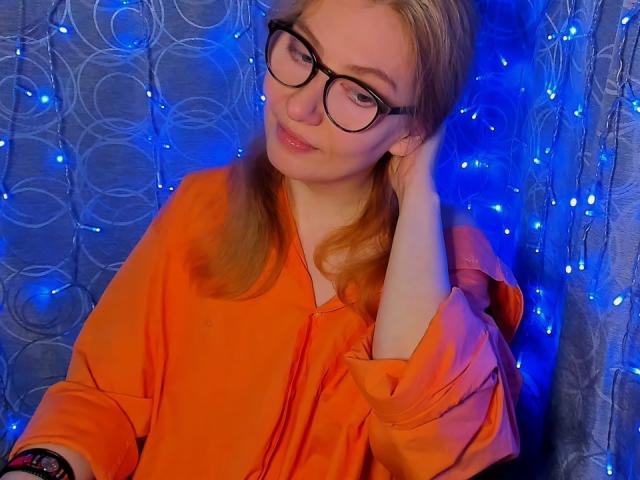 PaulinaSunny with glasses, orange shirt, blonde hair, hand on head, blue fairy lights, slight smile, wearing a black wristwatch, looking cute.