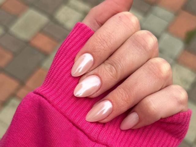 AlicePrings' hand with shiny, nude-pink, almond-shaped nails, wearing a bright pink rib-knit sleeve. Her skin is fair, and the background is blurred.