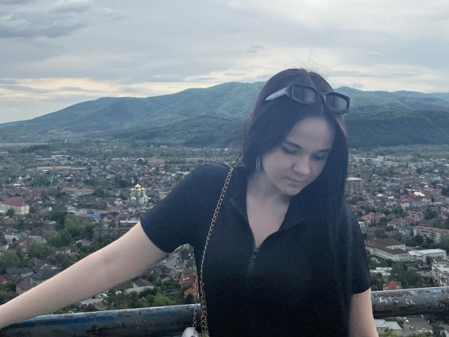 RoxyVesper with long black hair, wearing a black polo shirt, black sunglasses on her head, looking down, her ass slightly visible, standing by a rusty blue railing.