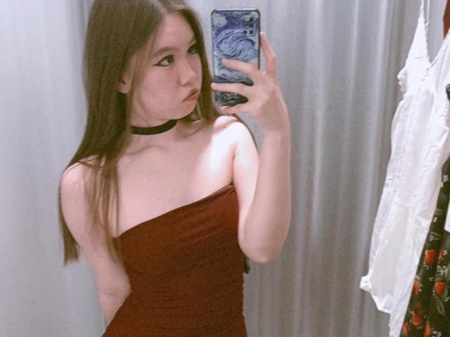 EmelineLattig with long brown hair, wearing a strapless red dress and black choker, taking a mirror selfie, showing her tits and pouty face, holding a phone with blue pattern.