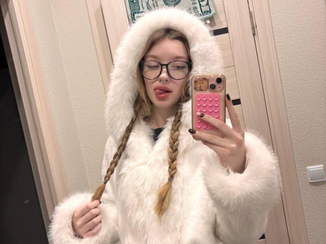 RossanaSemone with glasses, tongue out, wearing a fluffy white hooded coat, holding a pink phone with a textured back, braided hair, in a bathroom mirror selfie.