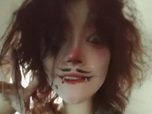 SophiaRenlay with messy brown hair, black eye makeup, and a silver lip piercing on her bottom lip, showing a slight smile. Her skin is pale, and she's looking forward.