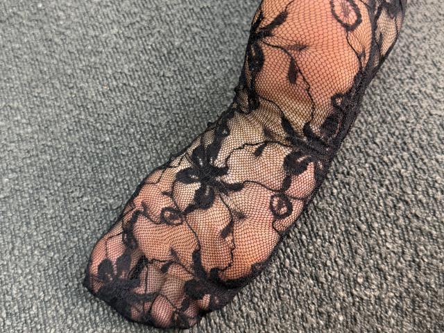 Tattiya's foot is covered in black lace, showing intricate floral patterns, with visible skin underneath the sheer, textured fabric. Her toes are slightly curled.