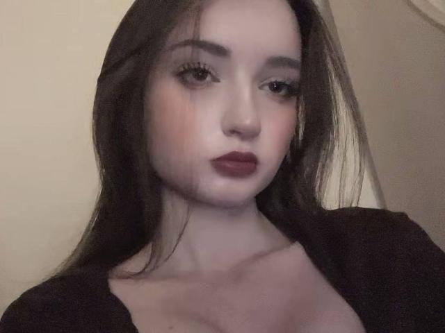 LatoshaGuarin has pale skin, dark brown hair, and red lipstick. She's looking at the camera with a slight smile, wearing a black top that reveals her small tits.