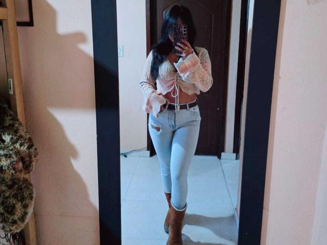 IsaLawrence has long black hair, a pink lace-up crop top, ripped light blue jeans, and brown boots. She's taking a mirror selfie, showing her toned midriff and ass.