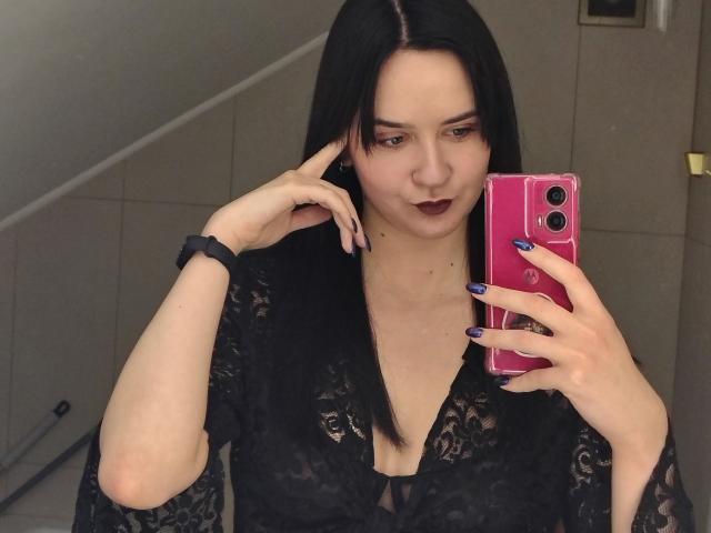 BerryDiva with black lace robe, purple nails, dark lipstick, holding pink phone, mirror selfie, black wrist scrunchie, straight black hair, pale skin, subtle smile, stairs in background.