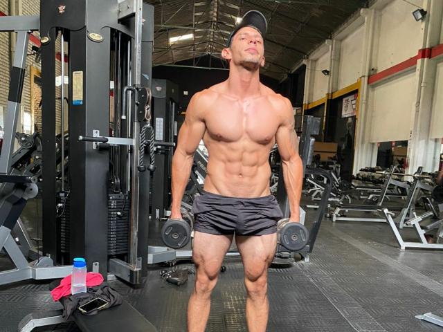 RobertHunk is a muscular dude with a toned ass, wearing black shorts and a cap, doing dumbbell exercises in a gym, with a strong, defined chest and abs.