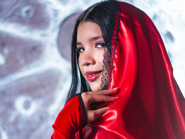 TaylorGil with shiny red satin, lace-trimmed headscarf, black hair, brown eyes, red lipstick, looking seductively at camera, right hand touching headscarf, sultry expression, glossy skin.