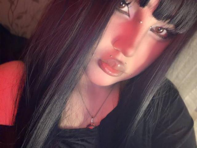 AlmaStampka a de longs cheveux noirs, des yeux marrons, du rouge à lèvres et de multiples piercings au visage. Elle porte un haut noir avec une épaule rouge. Sa peau est pâle..