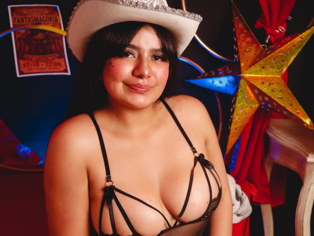 NicoleSamanta with medium tits in a black strappy bra, wearing a white cowboy hat, smiling, dark hair, light skin, and a small mole on her right cheek.