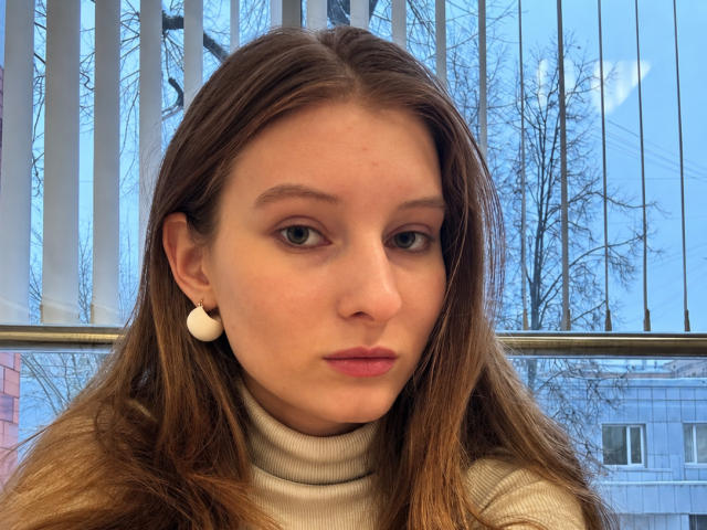 ArdelleCooksey has brown hair, light skin, and is wearing a turtleneck with white round earrings. She's pouting with pink lipstick, and her blue eyes are looking at the camera.