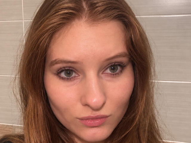 ArdelleCooksey's face, with her green eyes, long brown hair, and pink lips, staring directly at the camera. Her bare tits aren't visible, just her face.