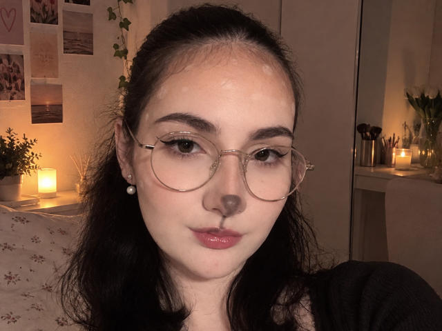 Ellaria has cum on her forehead, wearing glasses, with dark hair, pearl earrings, and red lipstick, looking at the camera with a slight pout. Her tits are not visible.