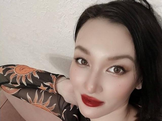 LanaJensenn tiene la piel pálida, ojos marrón oscuro, lápiz labial rojo y cabello negro. Lleva un vestido con estampado de sol y mira hacia arriba con una ligera sonrisa. Los senos son parcialmente visibles..