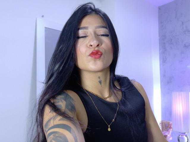 LuciadelaVega with long black hair, closed eyes, red lipstick, nose ring, tattoo on neck, black tank top, gold necklace, puffy lips, arm tattoo, soft purple lighting.