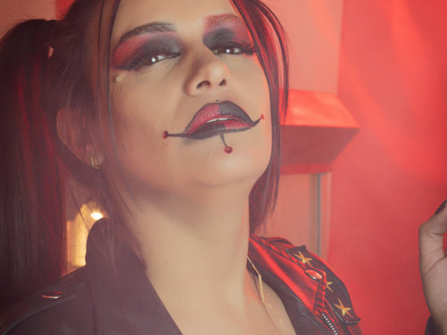 AriannaSeete with dark red lipstick, black eyeliner, and red eyeshadow. She has black lipstick with a red bead and a black pierced lip. Her hair is in a high ponytail.