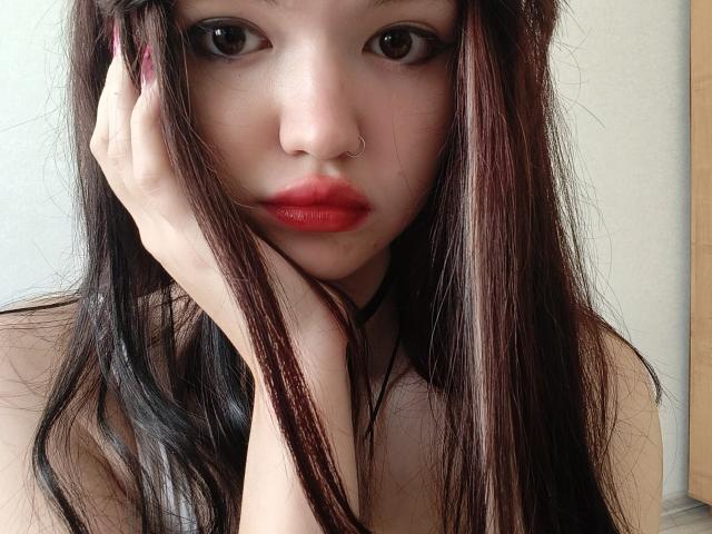 MistyEllstrom with long dark brown hair, red lipstick, nose ring, and hand on cheek, looking directly at camera, showing off smooth fair skin and subtle makeup.
