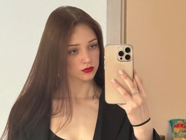 JoelleCalixte with long brown hair, red lipstick, and black top, holding a gold iPhone, taking a mirror selfie, showing her boobs and a ring on her right hand.