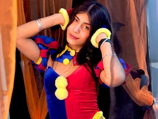 ValeryTranss with long black hair, smiling, wearing a red and blue velvet dress with yellow pom-poms, and yellow wristbands, holding her hair up. Her ass is cute.