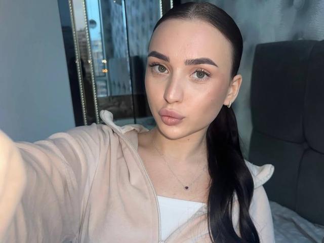 JaynaFeeler tem lábios carnudos, olhos verdes e um rabo de cavalo. Ela está vestindo um moletom rosa, e seus seios mal são visíveis por baixo do moletom. Ela está tirando uma selfie..