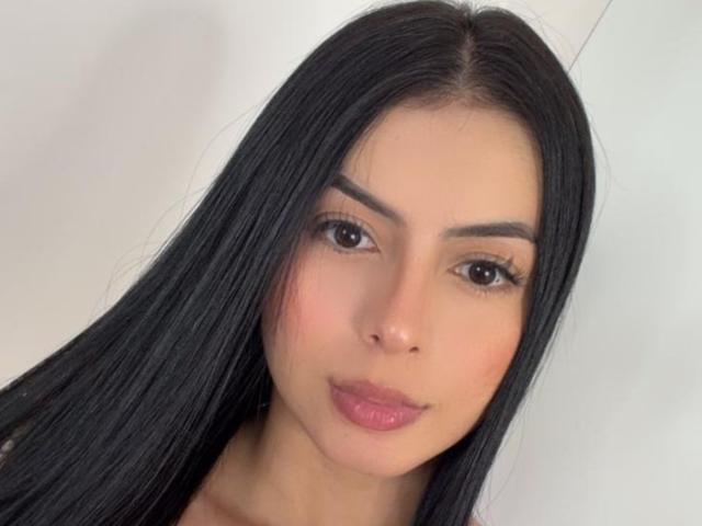 IsabellaJames has long black hair, brown eyes, thick eyebrows, and pink lipstick. She's looking straight at the camera with a slight smile, showing off her cute, sexy face.