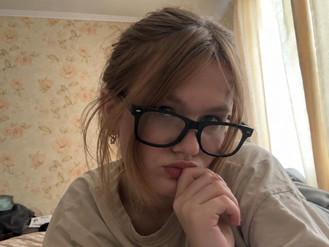 SeeOlausen, con le labbra corrugate, occhiali neri con montatura spessa e capelli biondi disordinati, appoggia il mento sulla mano, indossa una camicia beige, appare serio, con una luce naturale soffusa proveniente dalla destra..