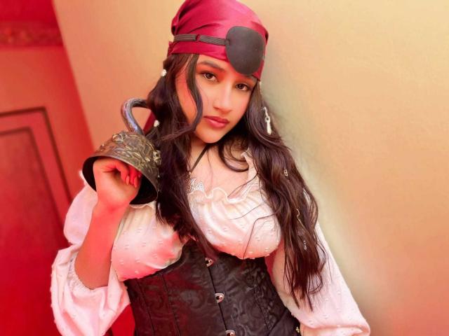 IrisBlair with long black hair, wearing a red hat, white blouse, black corset, holding a bronze bell, looking at the camera, soft red light, cute, sexy.
