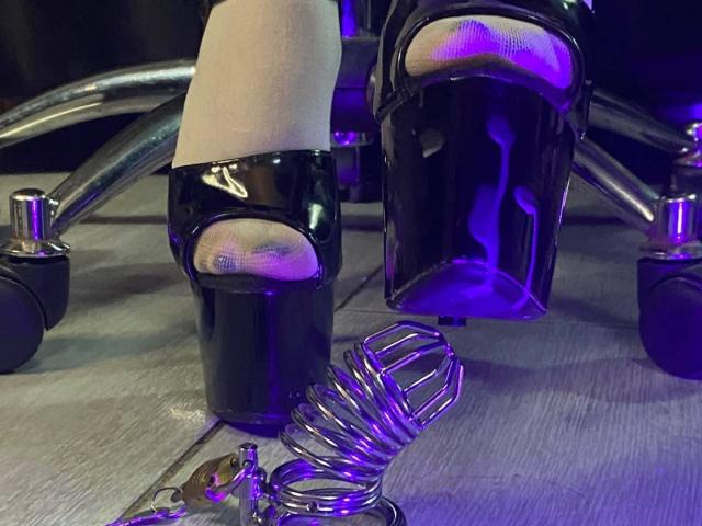 LilithStorm's feet in shiny black high heels with purple lights, exposing toes, and a metal ankle cuff on wooden floor. Metal cuff and keys in front.