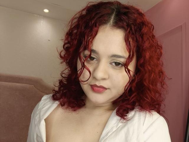 RosalieVittoria with curly red hair, fair skin, and pink lipstick, wearing a white shirt, showing small tits, slightly open collar, looking at camera with a subtle smile.