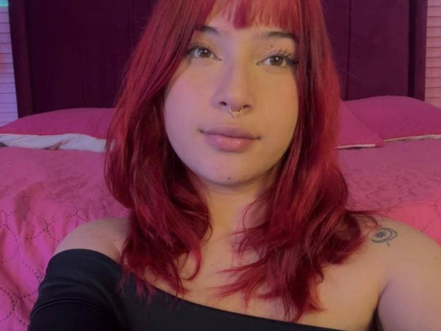 HaileyParck with red hair, nose ring, and black off-shoulder top, showing a small tattoo on her right shoulder, smiling slightly. Her tits are not visible.