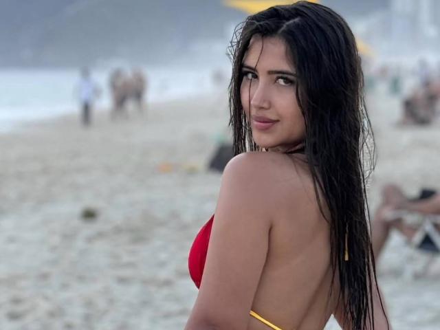 AnnaPooky with wet black hair, red bikini top, and tan skin, looking over her shoulder with a slight smile, showing her back and a hint of her ass.