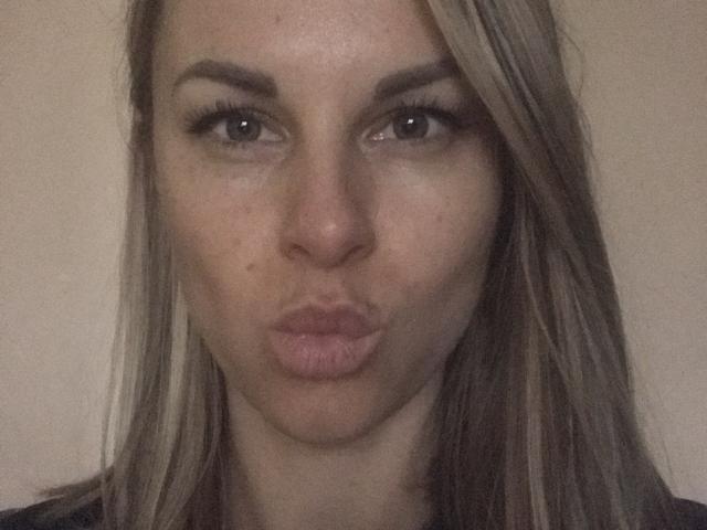 BelleLisaG's pouty face with slightly parted lips, green eyes, and blonde hair, showing a small zit on her nose, in a blurry selfie.