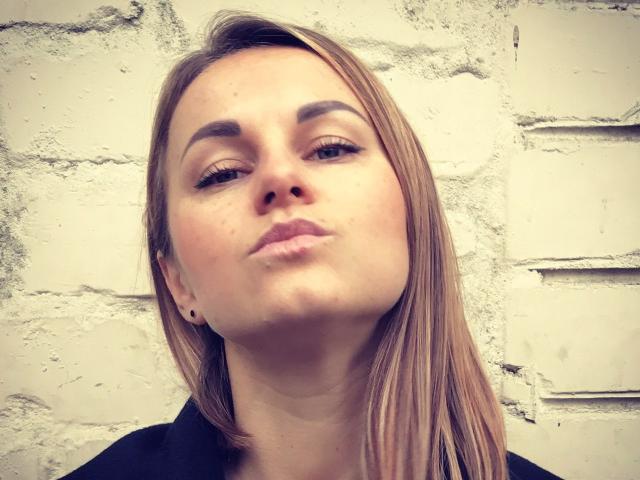 BelleLisaG has pouty lips, light brown straight hair, and a black earring in her left ear, looking slightly upward with a neutral expression.