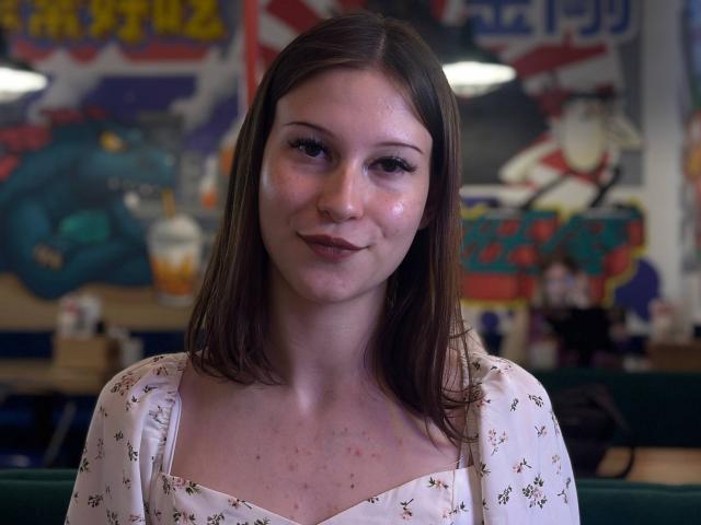 SharenMcdale has a cute, freckled face with light brown, straight hair. She's wearing a white floral dress, smiling slightly with a subtle blush on her cheeks.