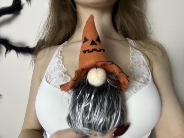 MiraRosse with a small gnomes plushie on her white lace bra. Gnome has an orange hat with a face and a fluffy white pom-pom. Boobs, lace bra.