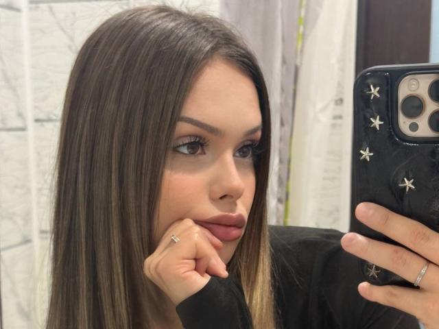 Delpha Herzfeld, con cabello castaño largo, labios rosados y un anillo en el dedo, sosteniendo un teléfono con calcomanías de estrellas, en un selfie frente a un espejo..