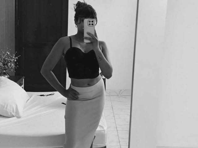 AshlyLee stands in a black strapless top and a tight, light-colored skirt, holding a phone to cover her face, with one hand on her hip, showing her small tits.