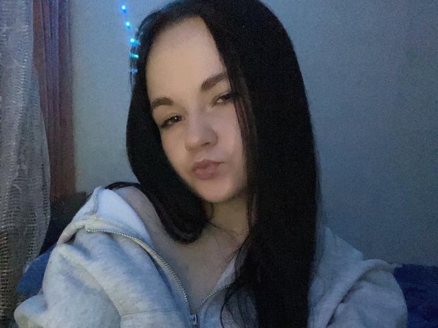 RoxyVesper has long black hair, light skin, and is wearing a grey hoodie. She's looking at the camera with a slight pout, and blue string lights are in her hair.