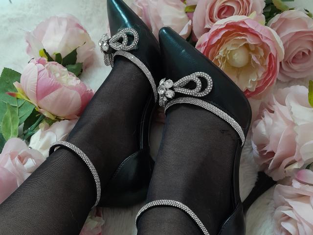 AmeliaMaiv's black, shiny high heels with silver rhinestone straps and small bows, covering her black pantyhose, surrounded by pink and white roses.