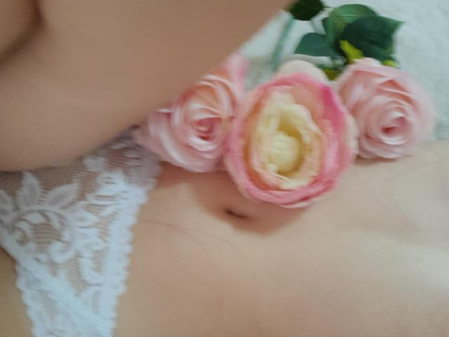 AmeliaMaiv's bare belly with pink roses and white lace, showing her navel and soft skin, slightly blurred, with green leaves in the upper right.