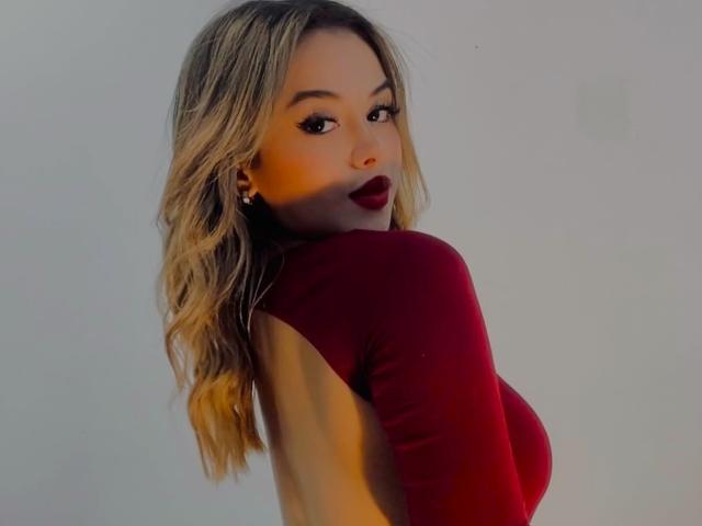 ZoeVibe with wavy blonde hair, wearing a red long-sleeve top, showing her back and looking over her shoulder with dark red lipstick, no visible tits or ass.