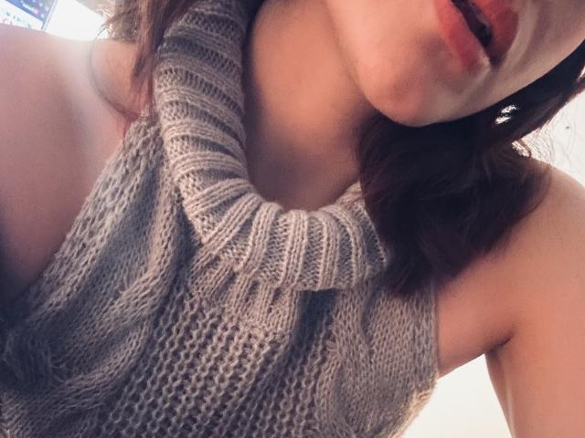SpencerLe with her mouth slightly open, wearing a grey, knitted, cowl-neck sweater, exposing her bare shoulders and upper chest. Her brown hair is partially visible.