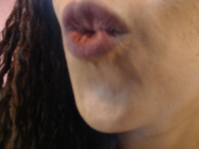 KenyaKarath's puffy, brownish-pink lips are slightly parted with a visible kiss mark, showing a bit of her dark brown, textured hair on the left side of the image.
